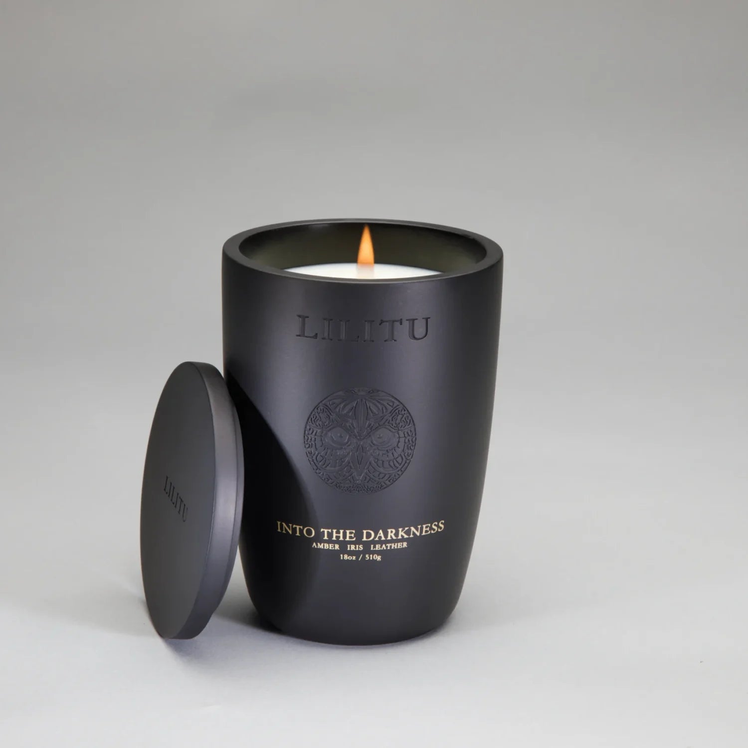 Lilitu Into the Darkness black ceramic candle, lit, with its lid resting against the vessel